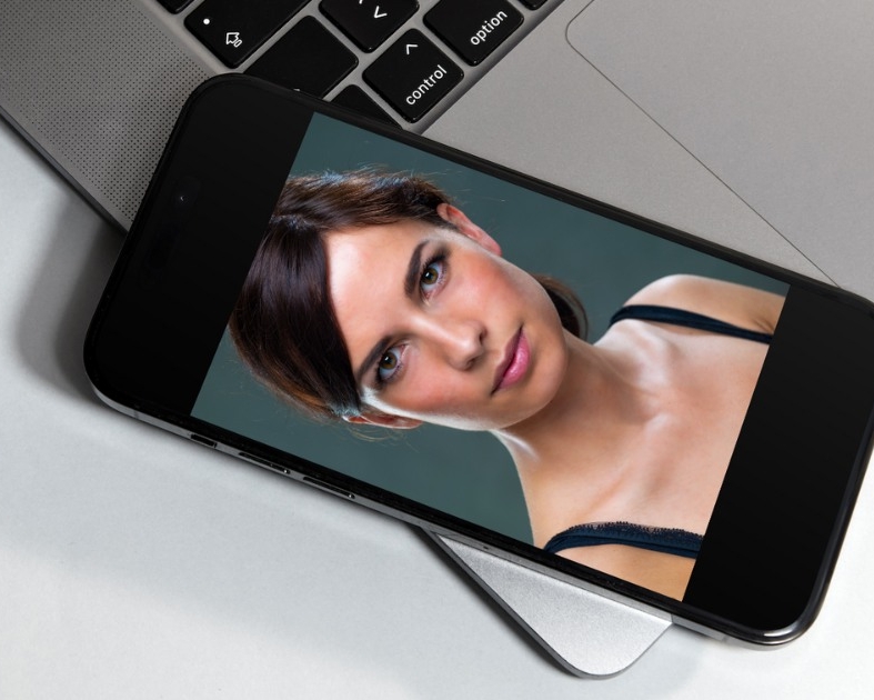 Ein Smartphone mit einem Foto einer jungen Frau auf einem Smartphone liegt auf einem offenen MacBook - Beitragsbild zum Artikel Bildrecht und Urheberrecht